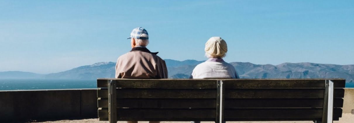 man and woman sitting on bench facing sea